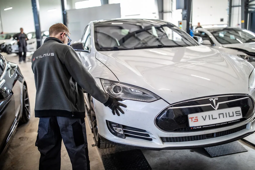 Meistras apžiūri balto Tesla Model S priekinę kėbulo dalį „TS Vilnius“ servise